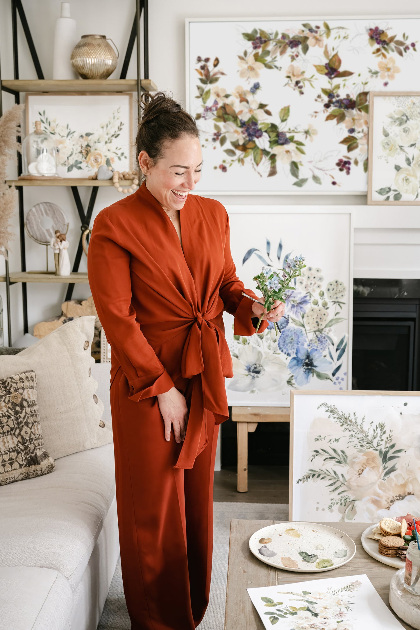 Artist Tonya Cruz wearing burnt orange outfit surrounded by beautiful floral artworks